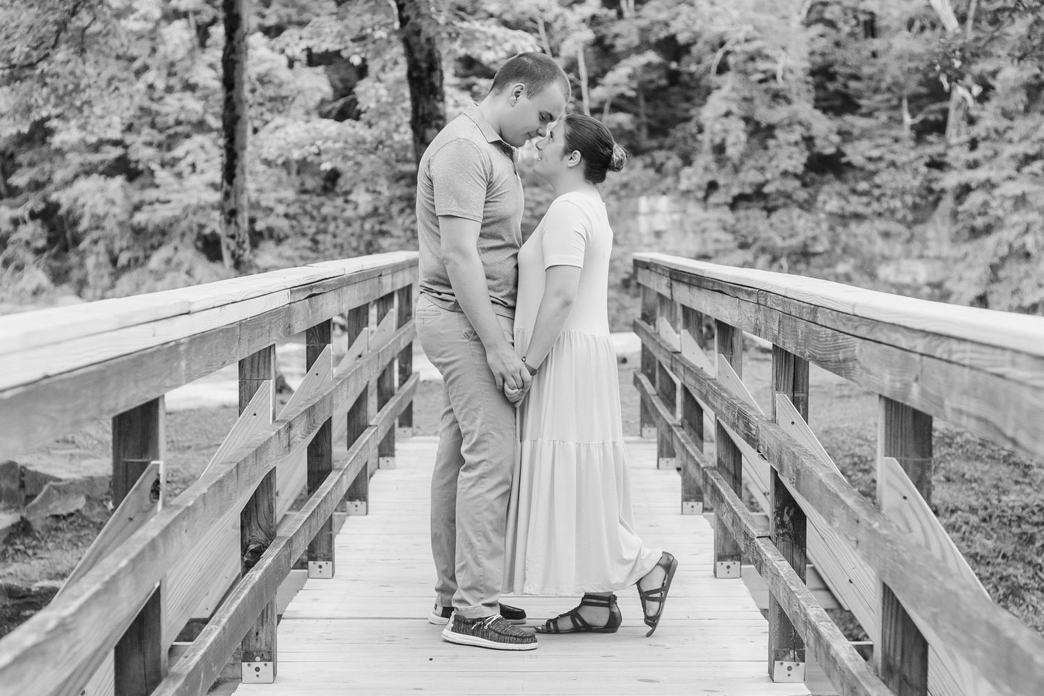 A couple poses on a rustic wooden bridge in a romantic black and white photograph.