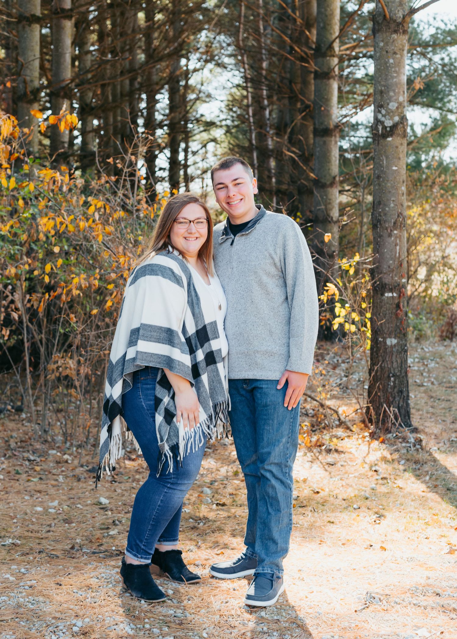 Couple in casual wear walking together through a wooded path with autumn foliage in the background.