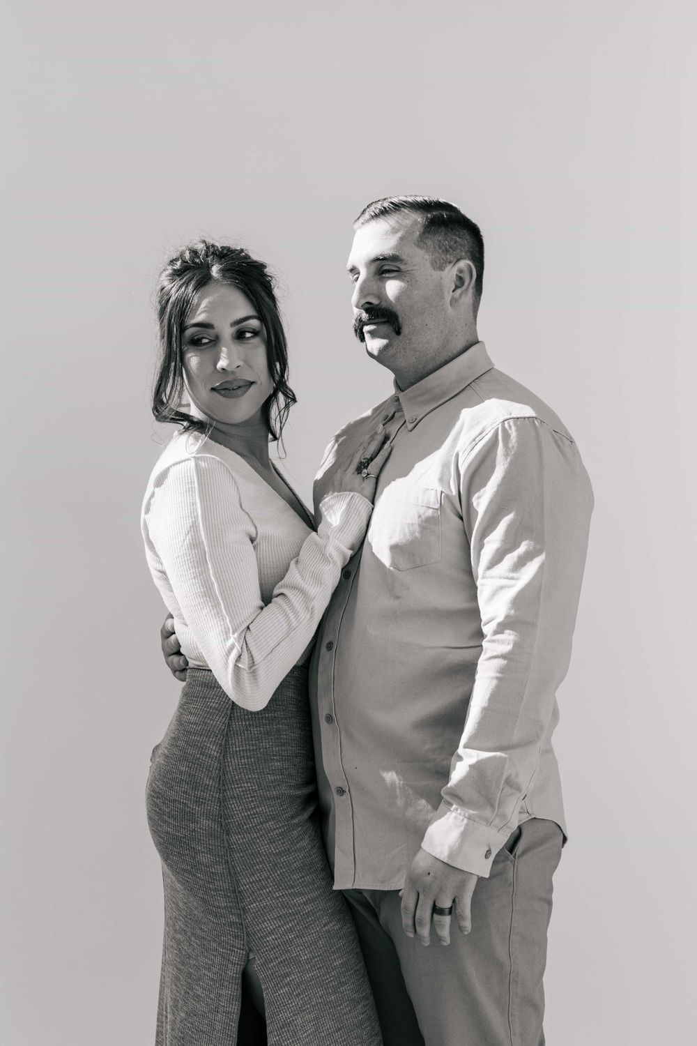 Black and white portrait of a stylish couple posing together against a white background.