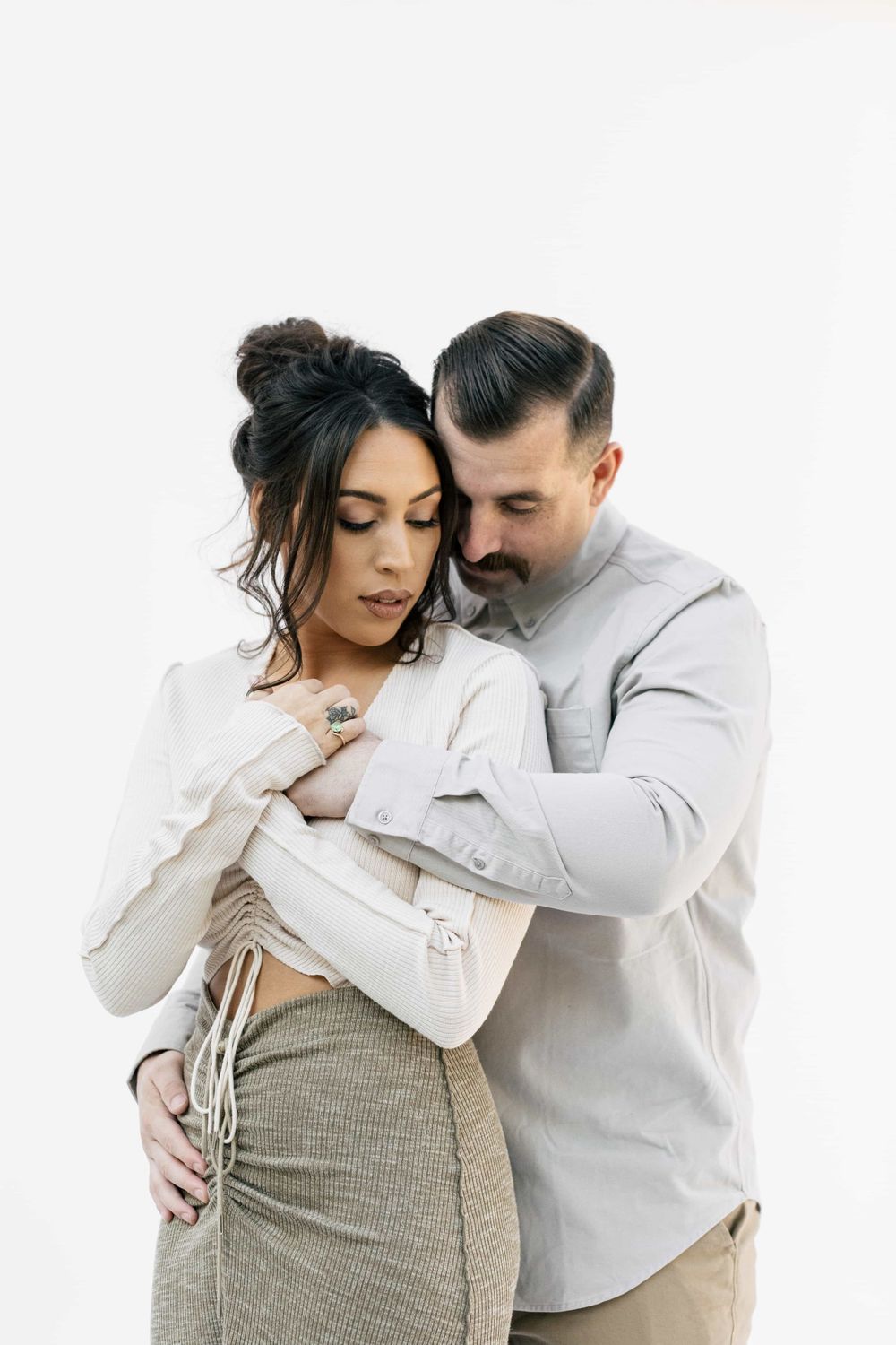 Man embracing woman from behind in a tender couples portrait on white background.