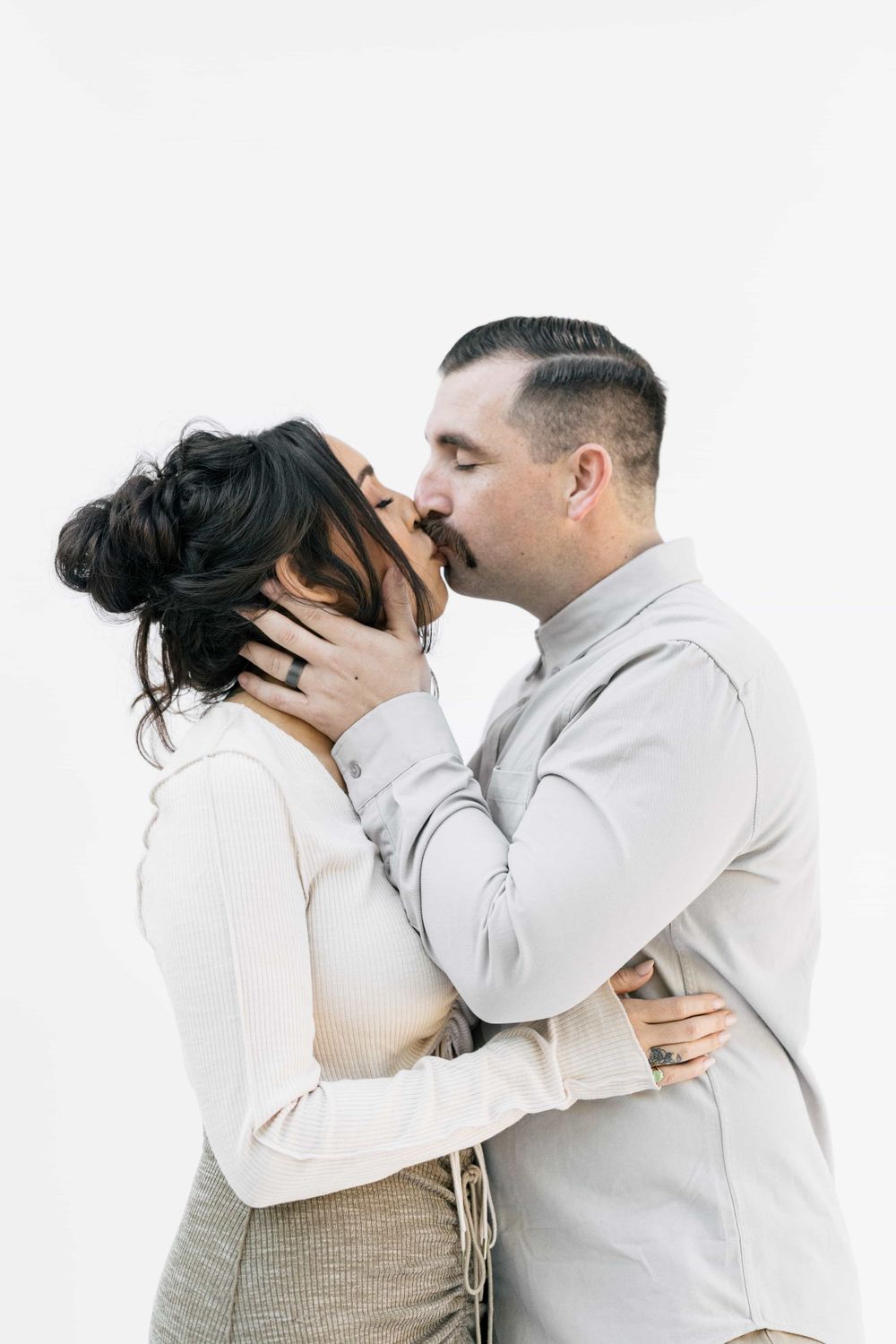 A couple shares a romantic kiss, the man tenderly holding the womans face against a white backdrop.