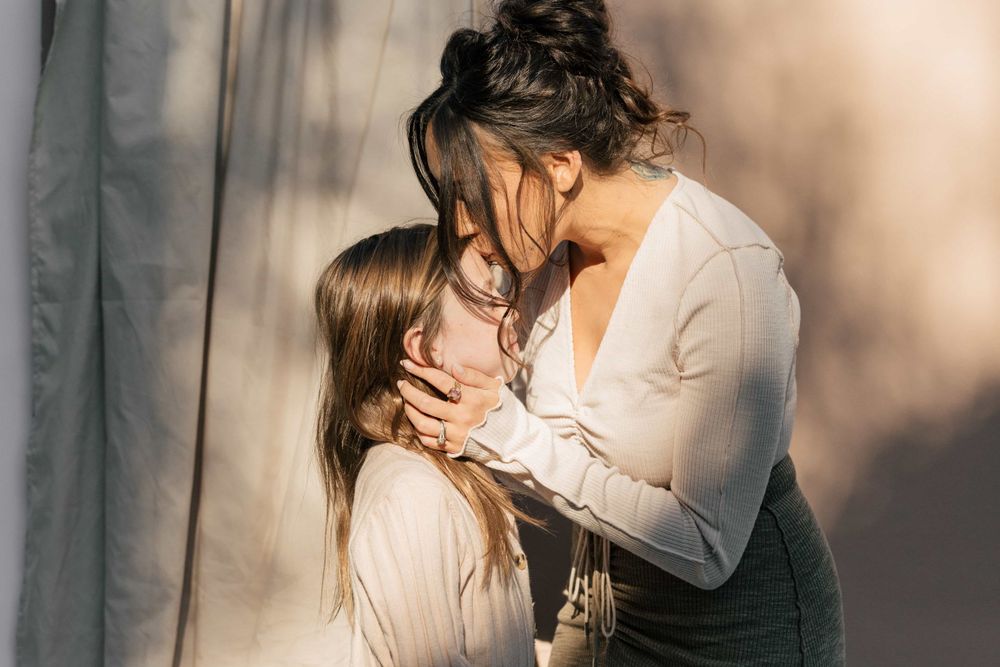 Loving mother gently holding daughter's face in a warm, intimate moment outdoors.