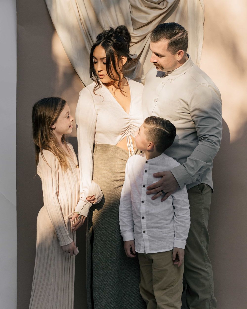 Family of four sharing a tender moment together against a draped fabric backdrop.