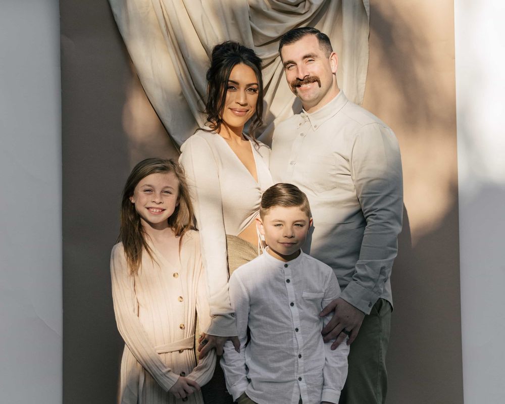 Happy family portrait with parents and two children smiling before a draped background.