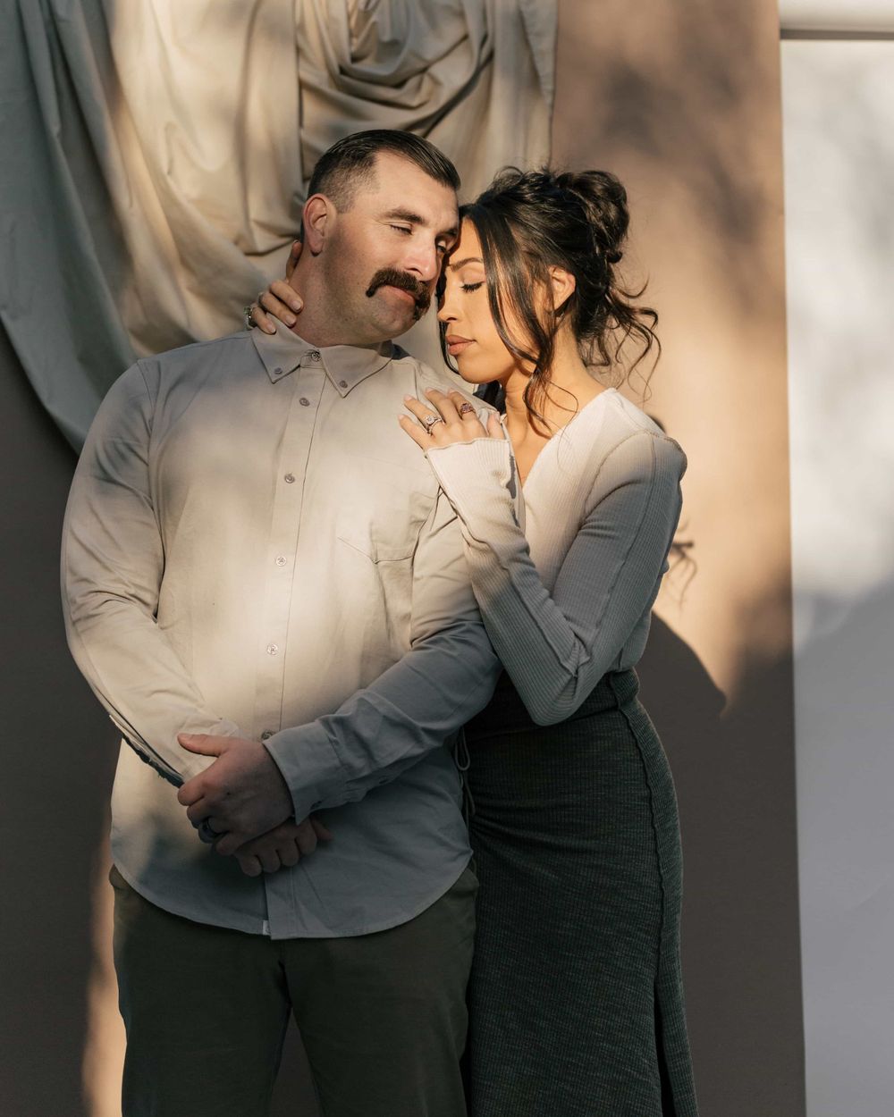 Couple sharing an intimate embrace against a draped fabric backdrop in golden sunlight.
