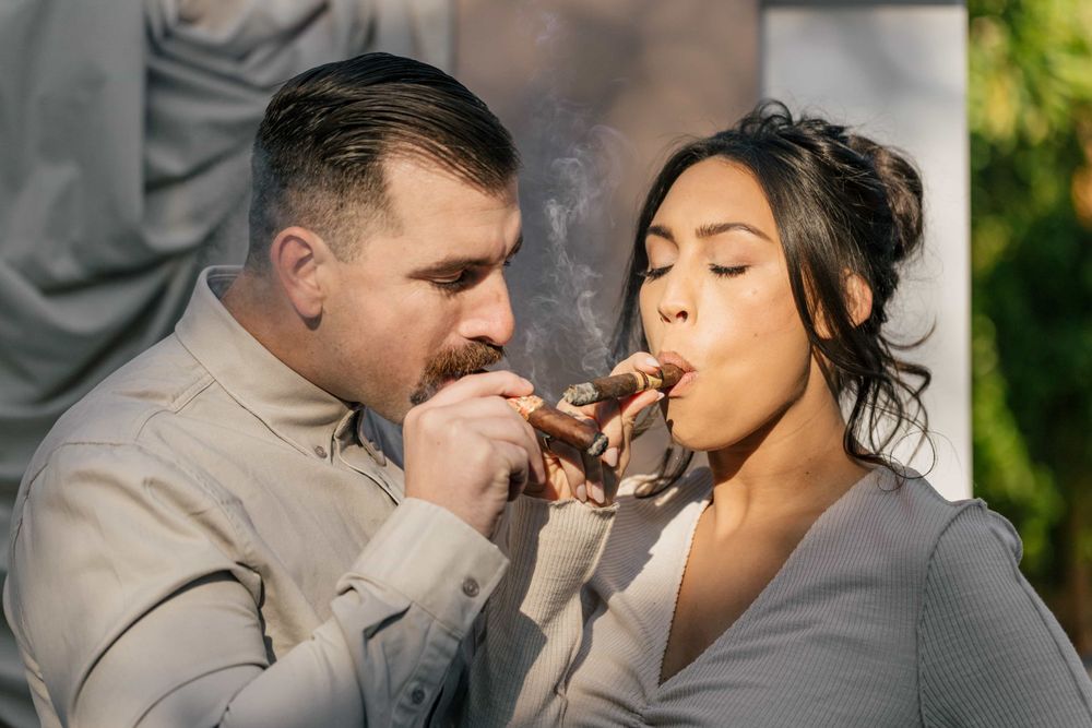 Couple sharing a cigar together outdoors in a playful, candid moment.