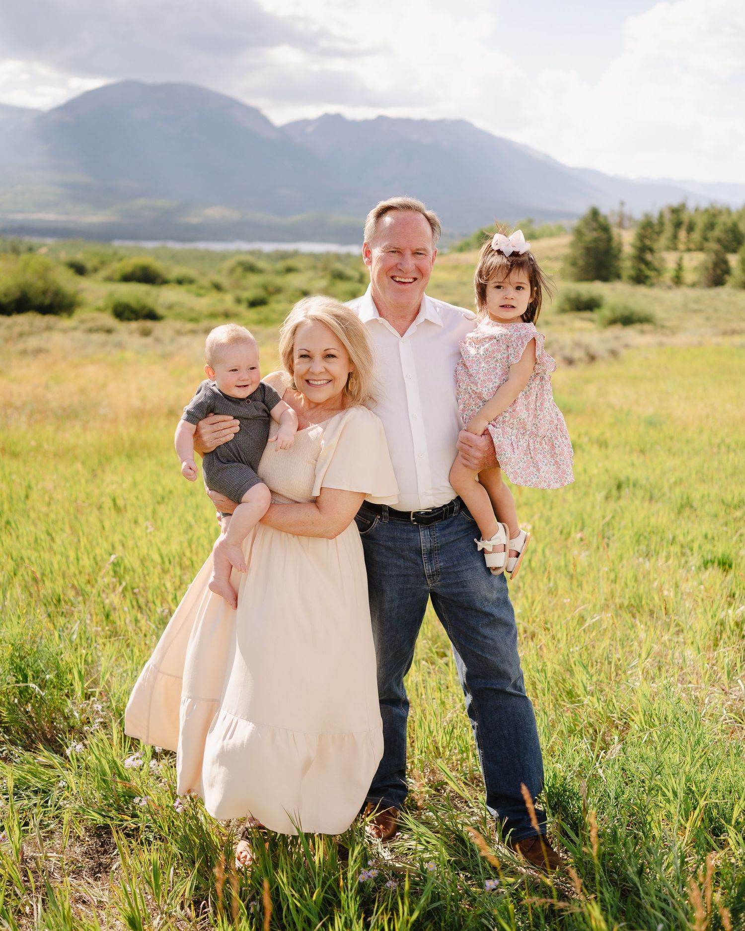Family portrait in a scenic mountain meadow with tall grass and mountains in the background.