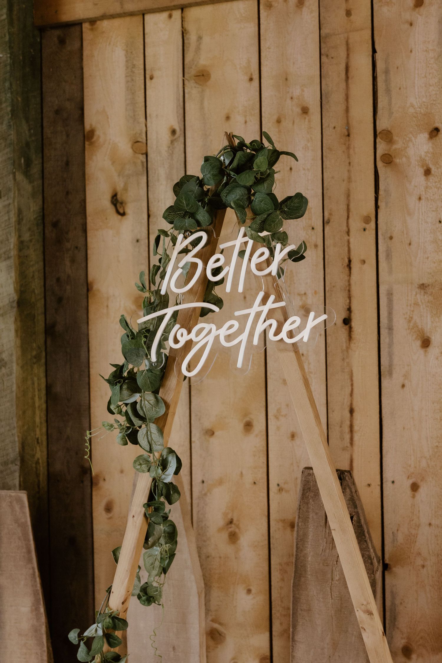 White 'Better Together' neon sign mounted on wooden wall with green ivy decoration.