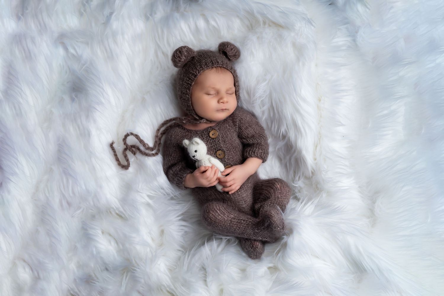 Sweet newborn portraits with teddy bear accessories on white fur backdrop.