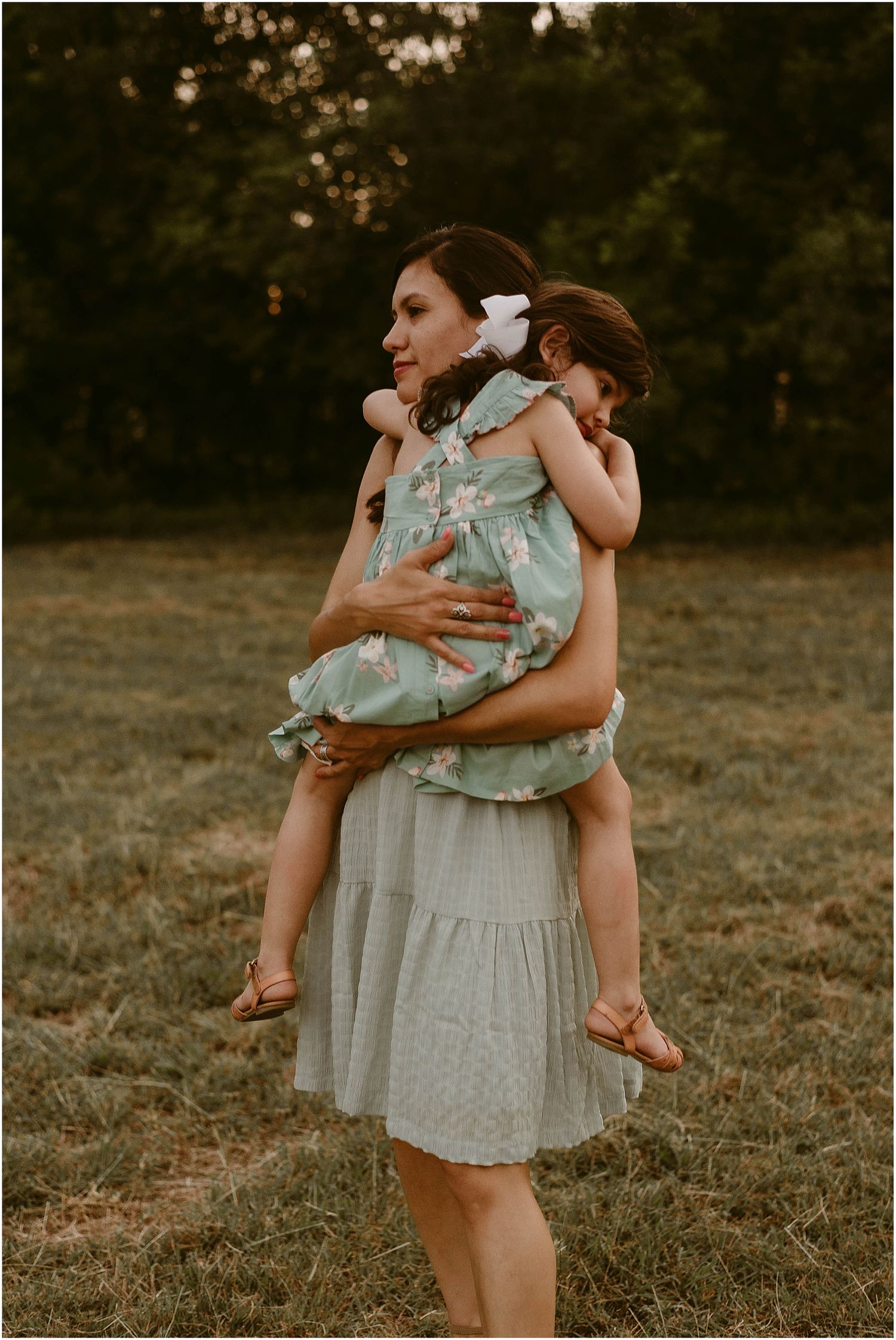 A tender moment captured as a child rides piggyback in a mint green dress at dusk.
