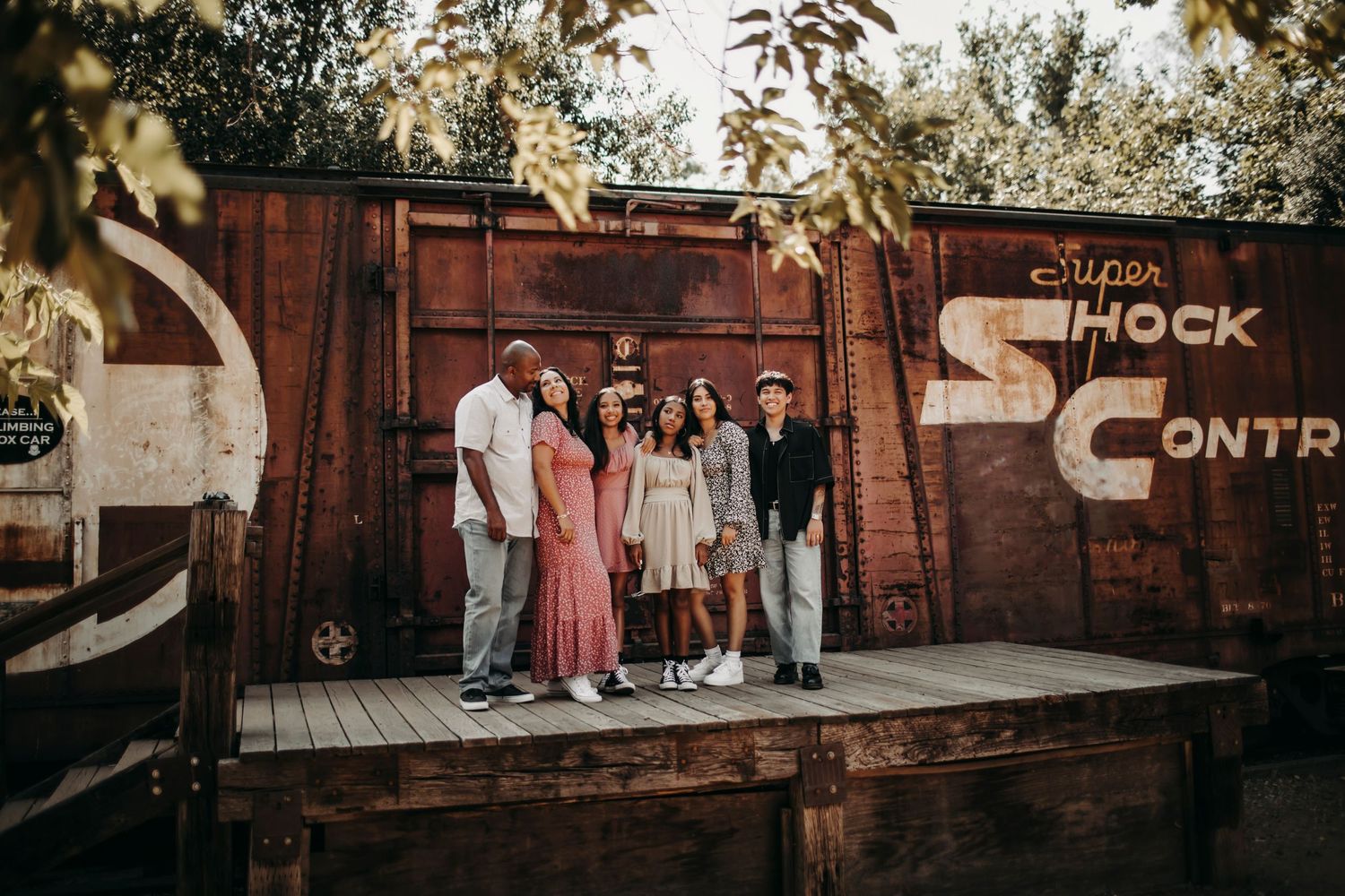 A family with older children posing together in front of a vintage train car, smiling warmly and enjoying a timeless, nostalgic moment.