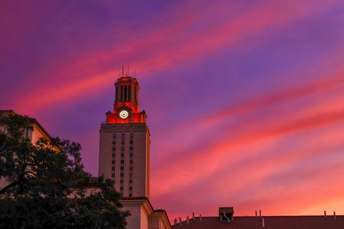 University tower silhouetted against dramatic purple and pink sunset sky.