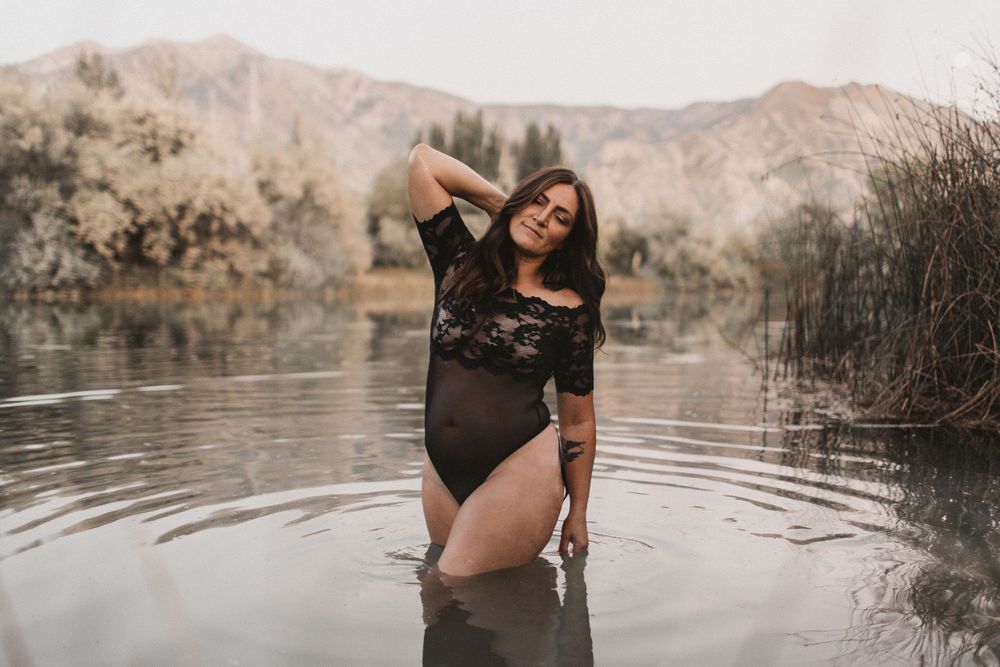 A person in a black swimsuit poses in a serene mountain lake with reflective water.