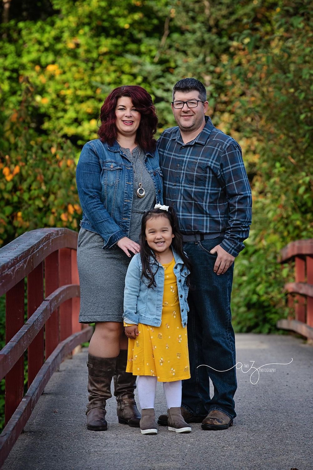 Family of three poses together on wooden bridge during autumn photo session.