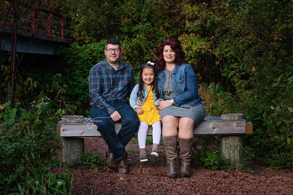 Family dressed in casual attire sits together on wooden bench in forest setting.