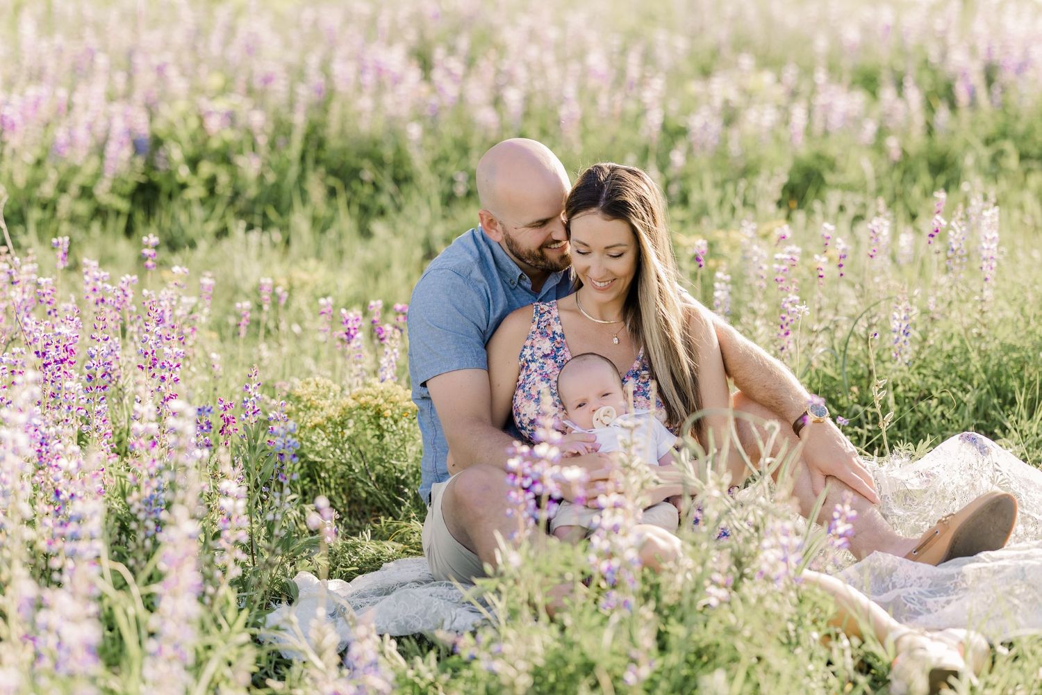 A couple shares an intimate moment while sitting in a field of purple wildflowers.