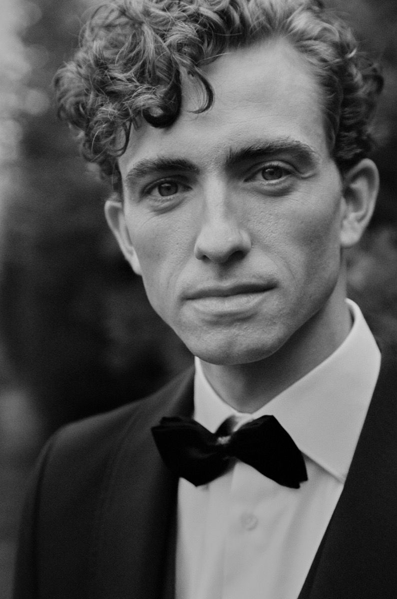 Black and white portrait of a person in formal attire with bow tie and curly hair.