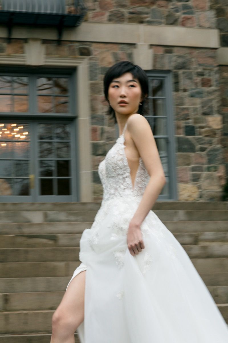 Bride in lace wedding gown poses on stone steps of historic building with dramatic movement.