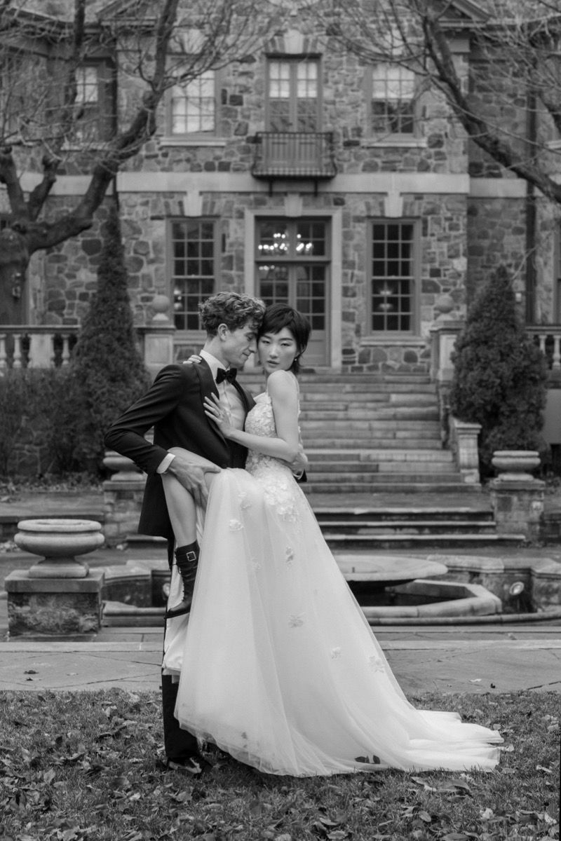 A romantic black and white wedding photo of a couple embracing on stone steps of a historic building.