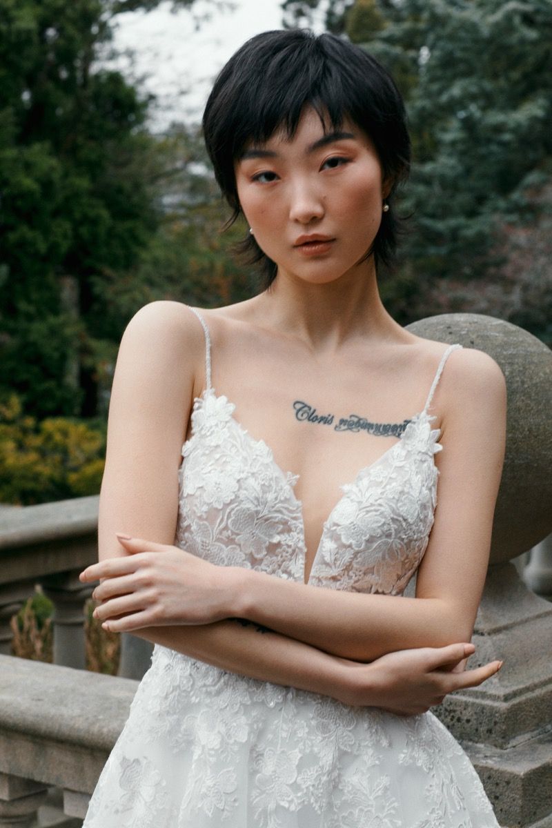 A bridal portrait showcasing a detailed white lace wedding dress with plunging neckline against outdoor scenery.