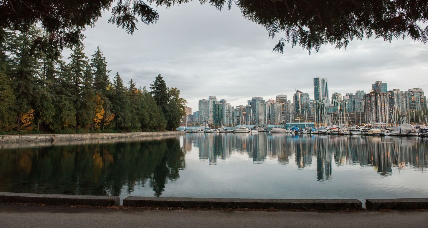 Vancouver skyline reflects in the calm waters of Stanley Park with fall foliage in the foreground.
