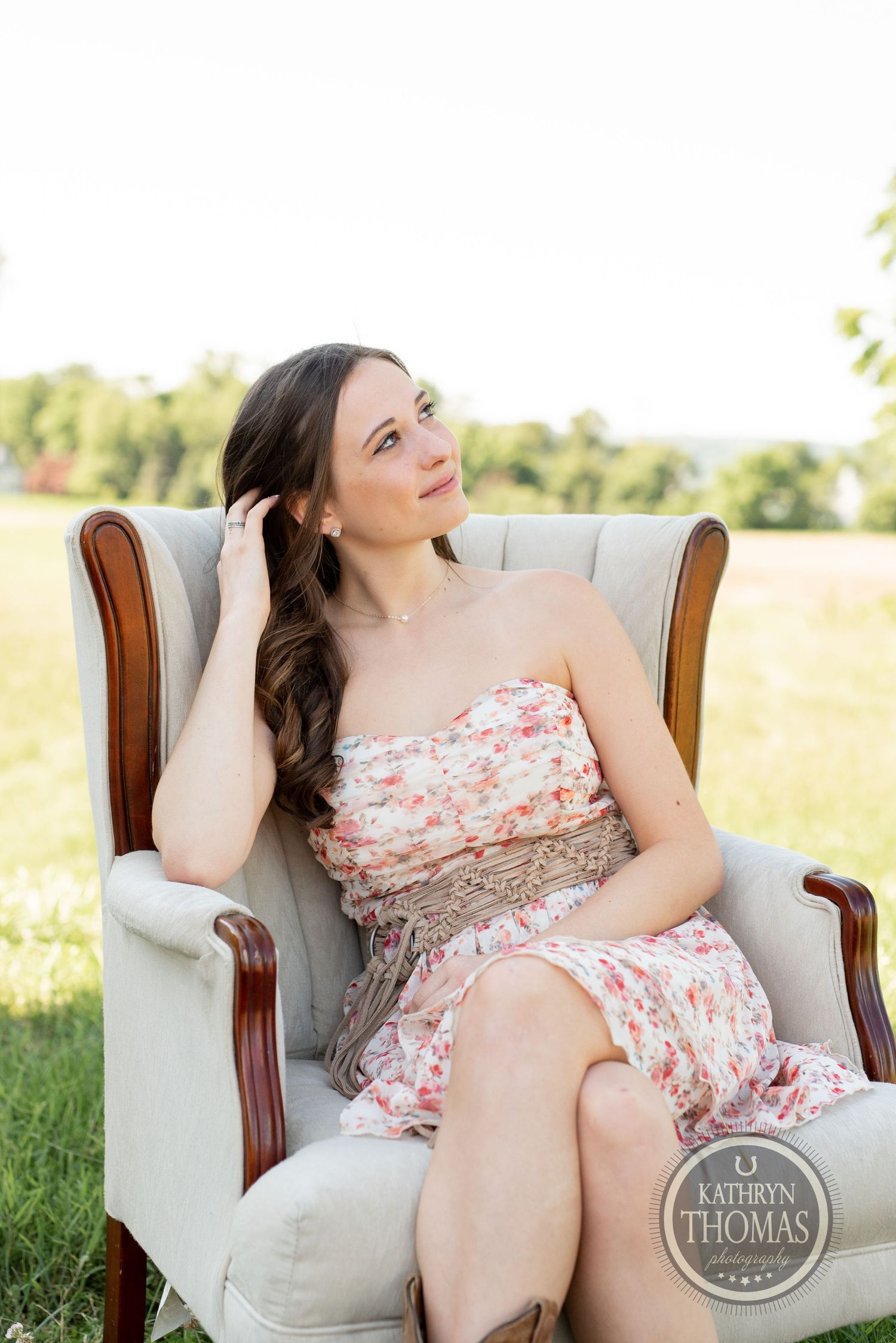 Natural light portrait in cream armchair wearing strapless floral dress.