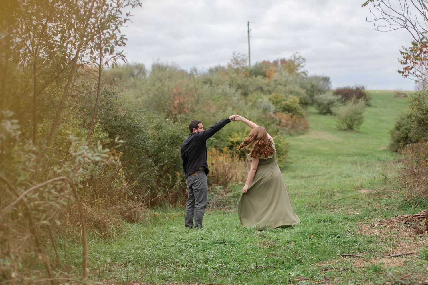 Couple walking together through a scenic autumn field with fall foliage in the background.