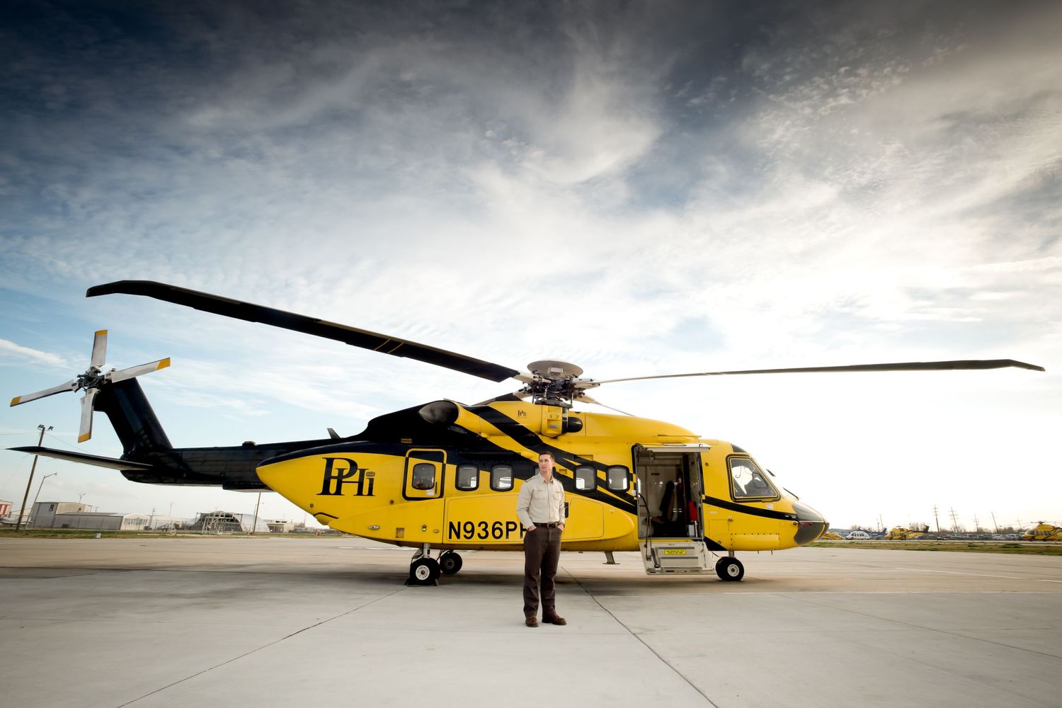 Yellow rescue helicopter parked on tarmac under dramatic cloudy sky.