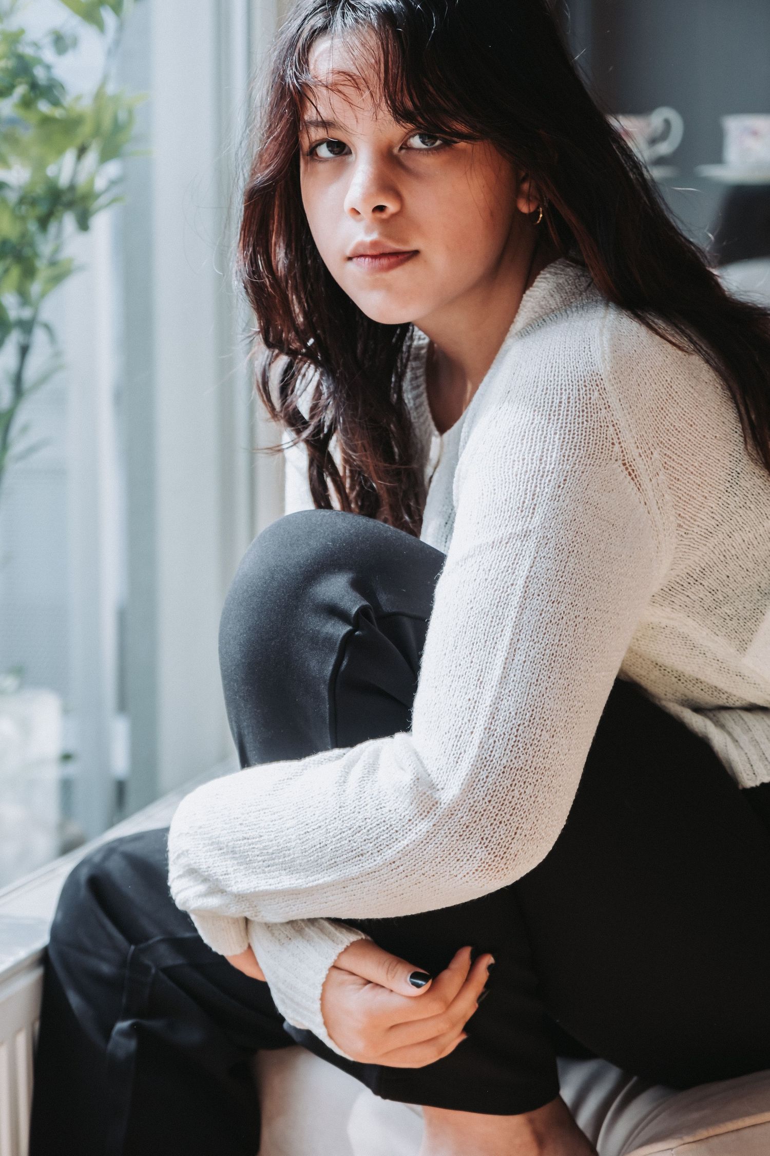 Person in white sweater sits contemplatively by window.