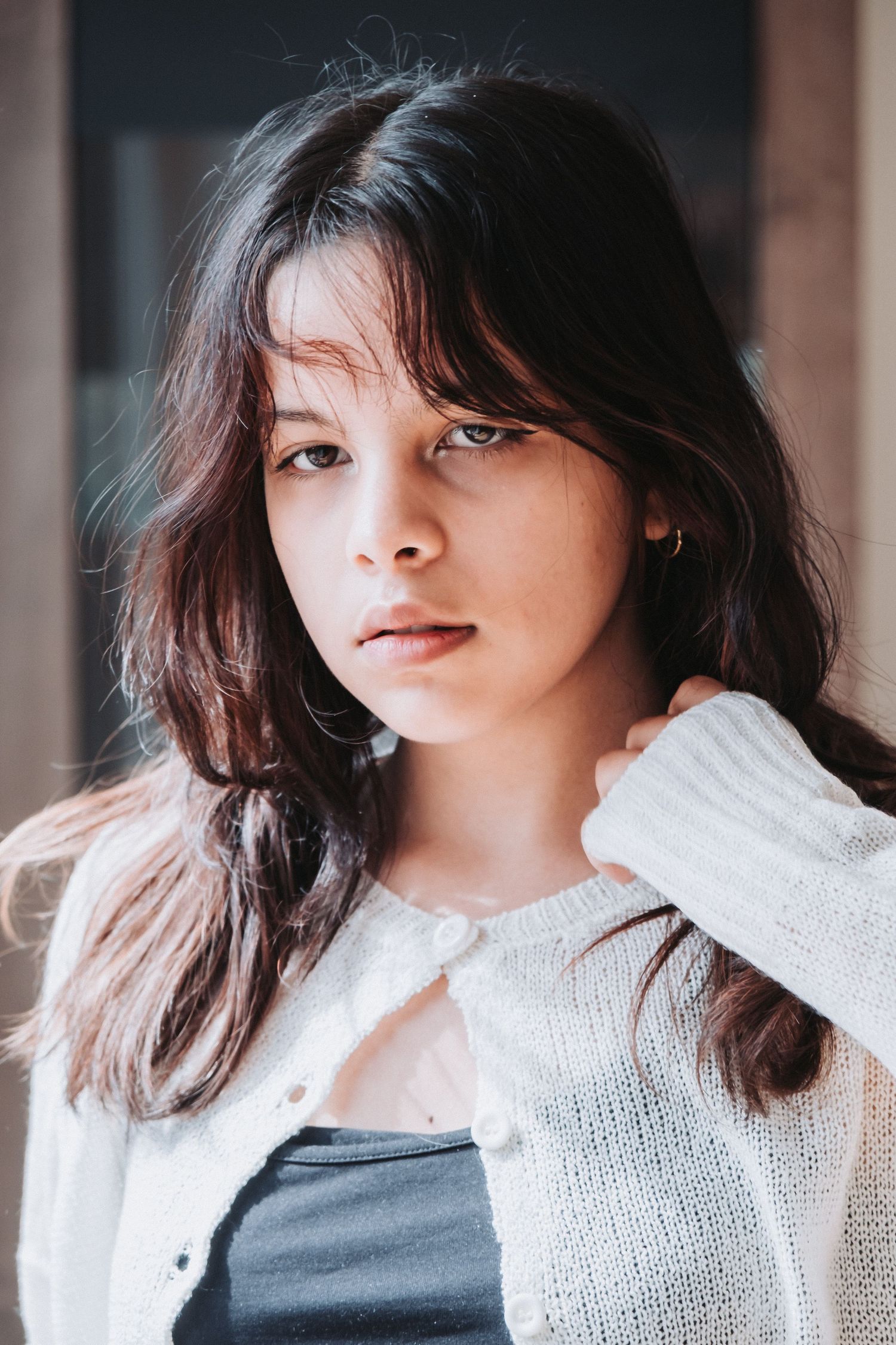 Portrait of woman wearing white cardigan against dark background with soft natural lighting.