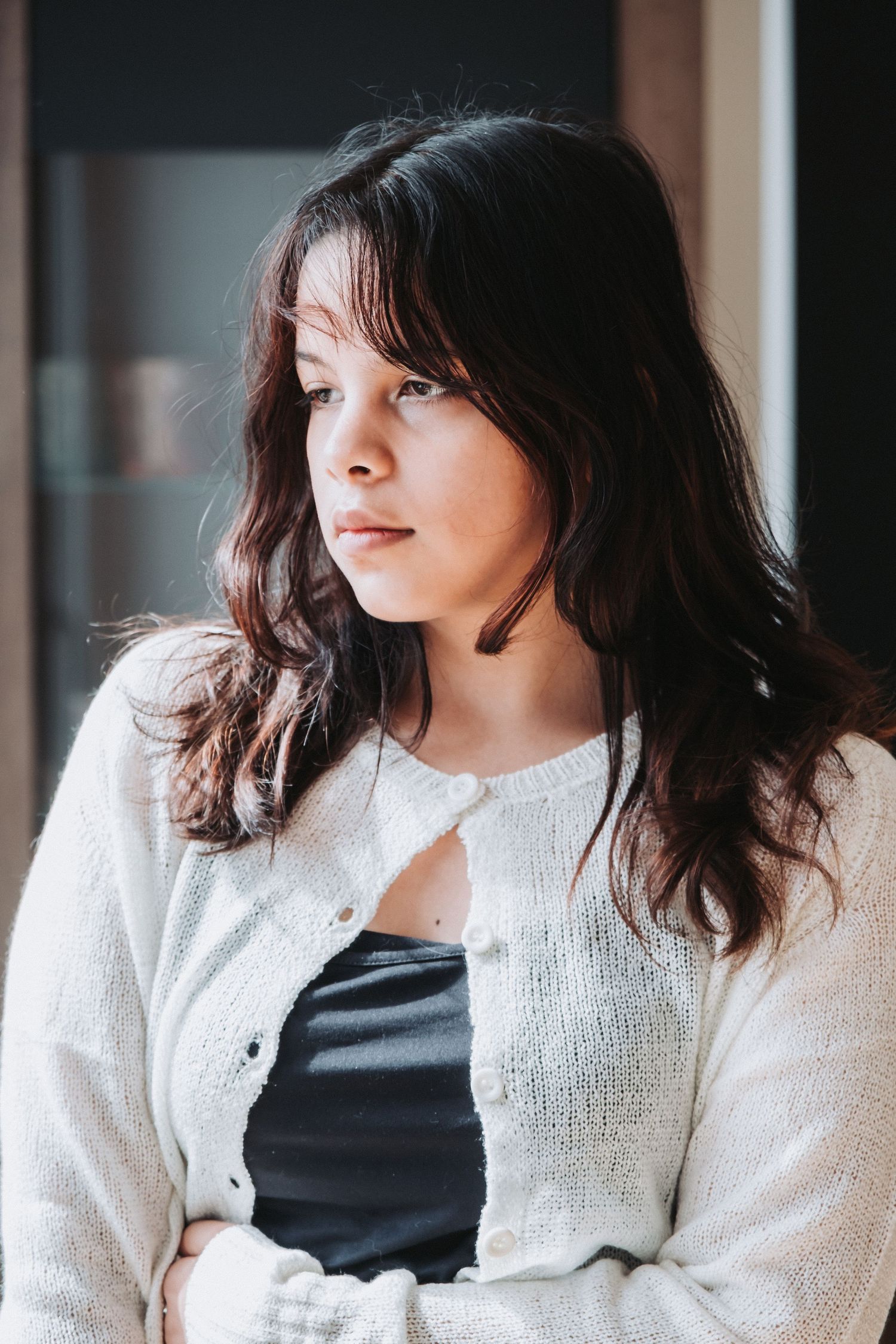 Person in white cardigan and dark top poses against natural lighting.