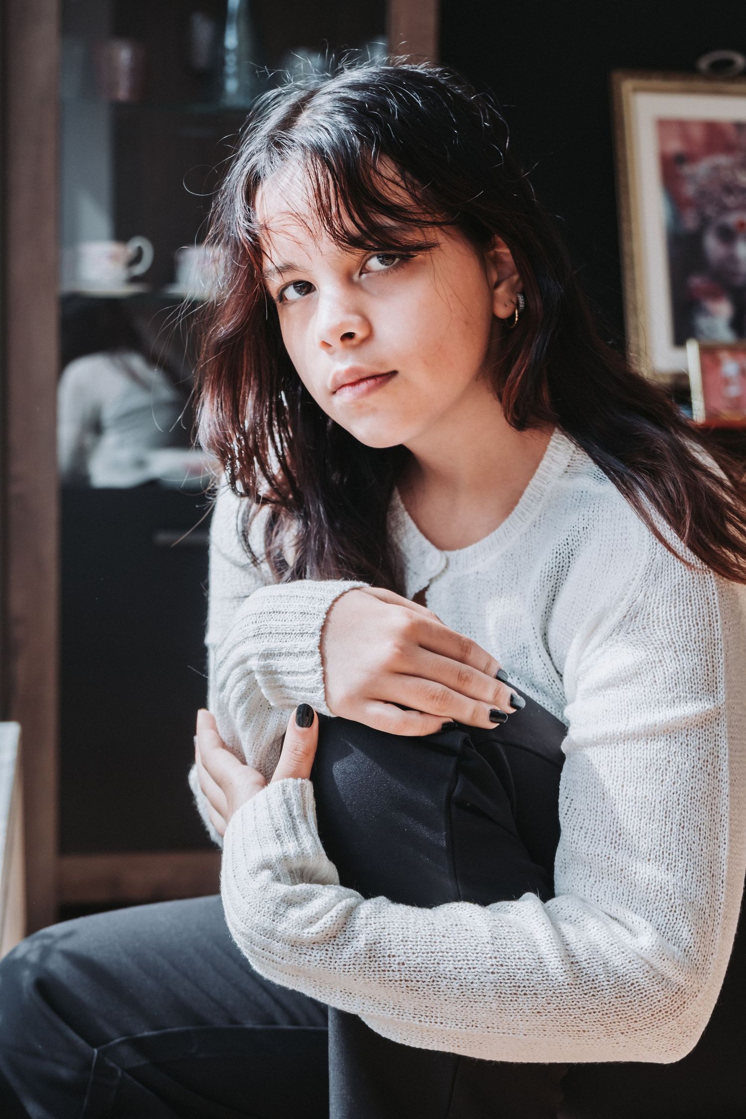 Indoor portrait featuring long dark hair and cream colored sweater against a shadowy background.