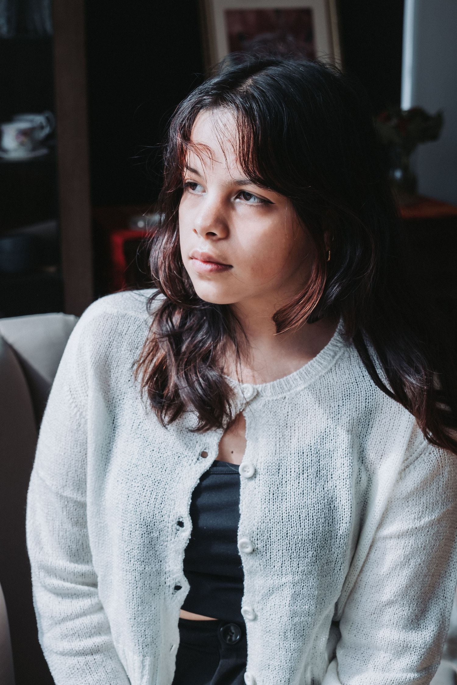 Person in white knit cardigan and dark top poses in indoor setting.