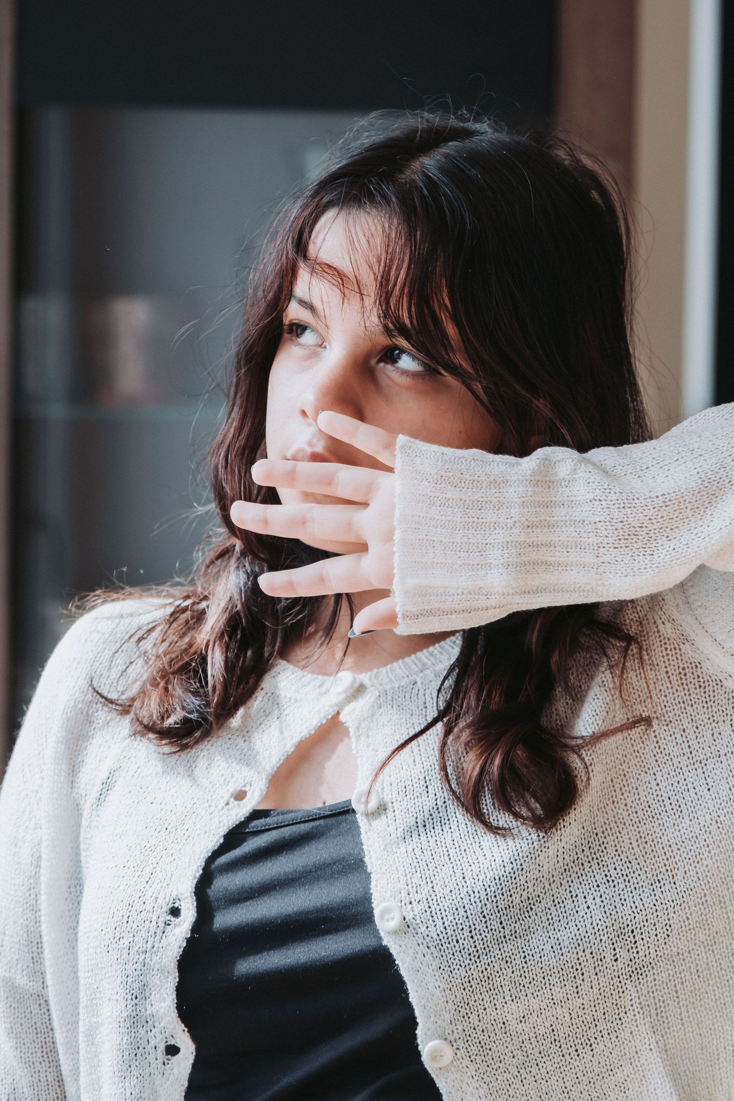 Woman in white cardigan covering mouth with sleeve in artistic portrait.