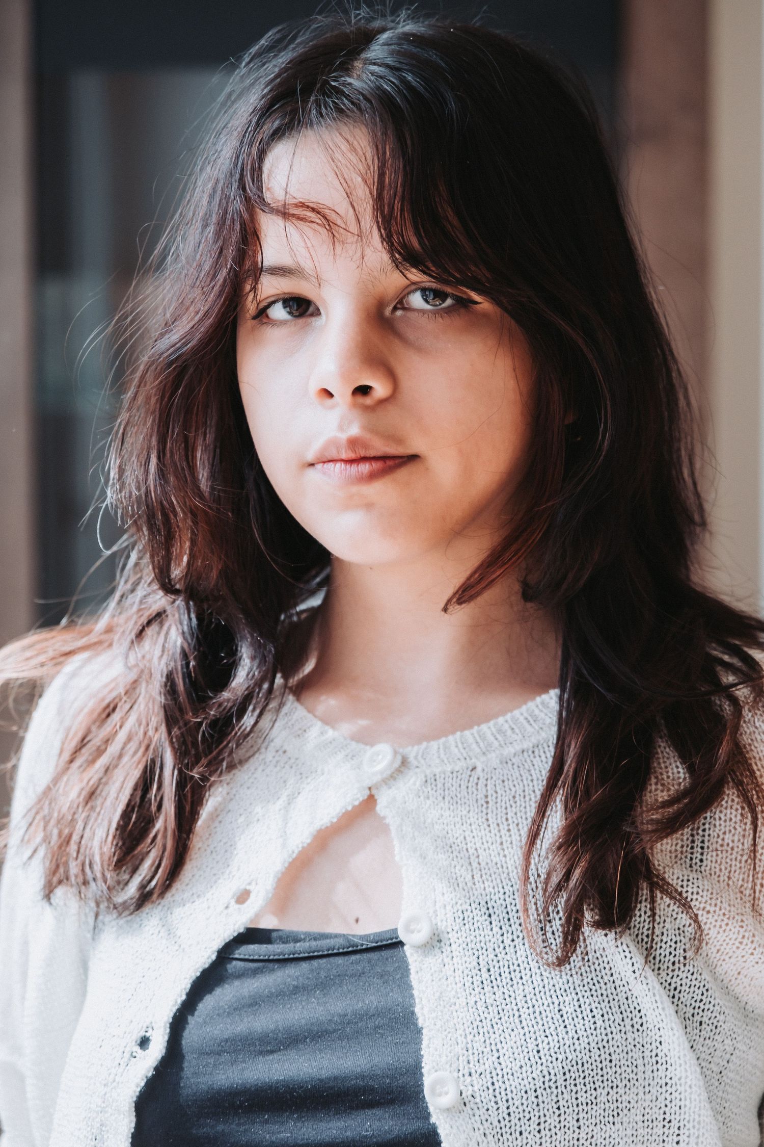 Woman in white button-up sweater poses against dark background in natural light portrait.