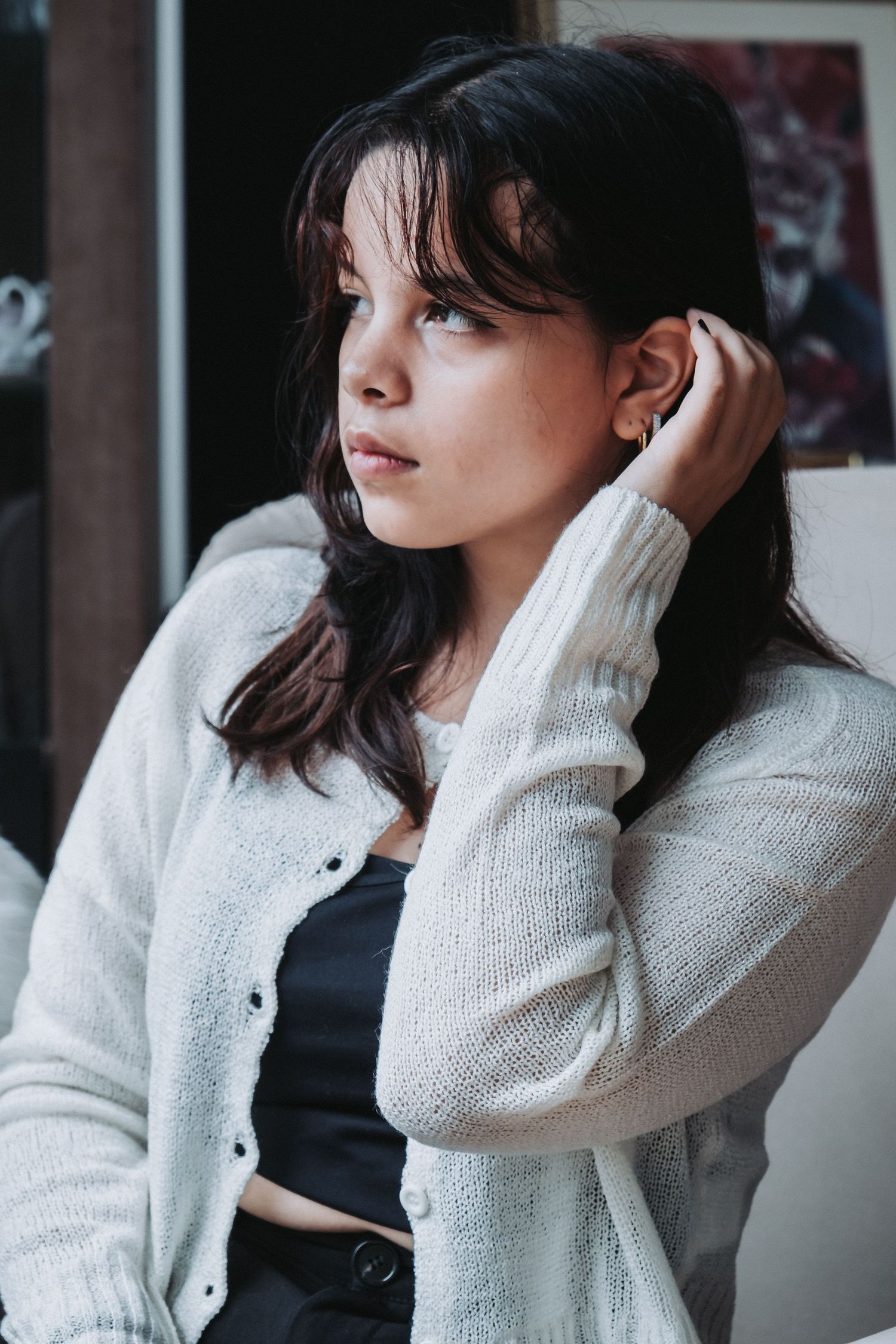 Person in white cardigan and dark top poses against indoor background.