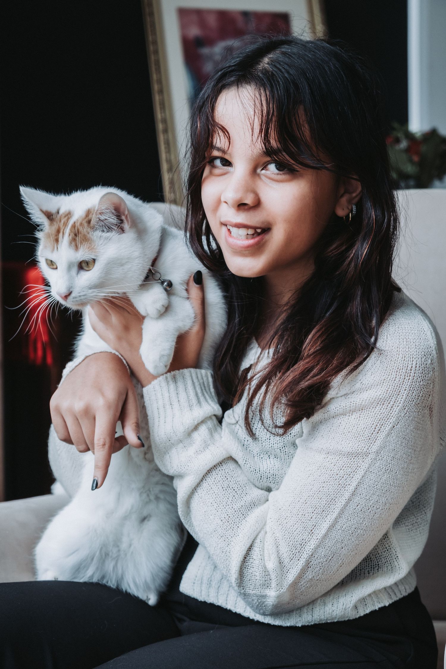 Woman in white sweater holding white cat while sitting on couch in natural light.