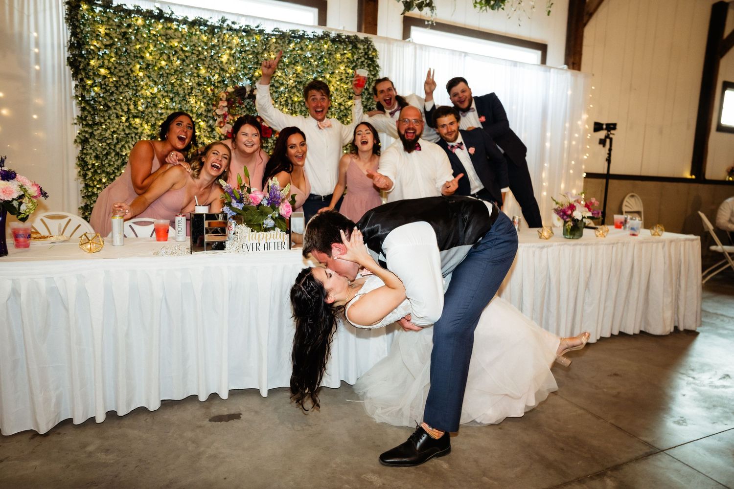 Couple performs dramatic dip dance move during wedding reception as guests cheer from head table.