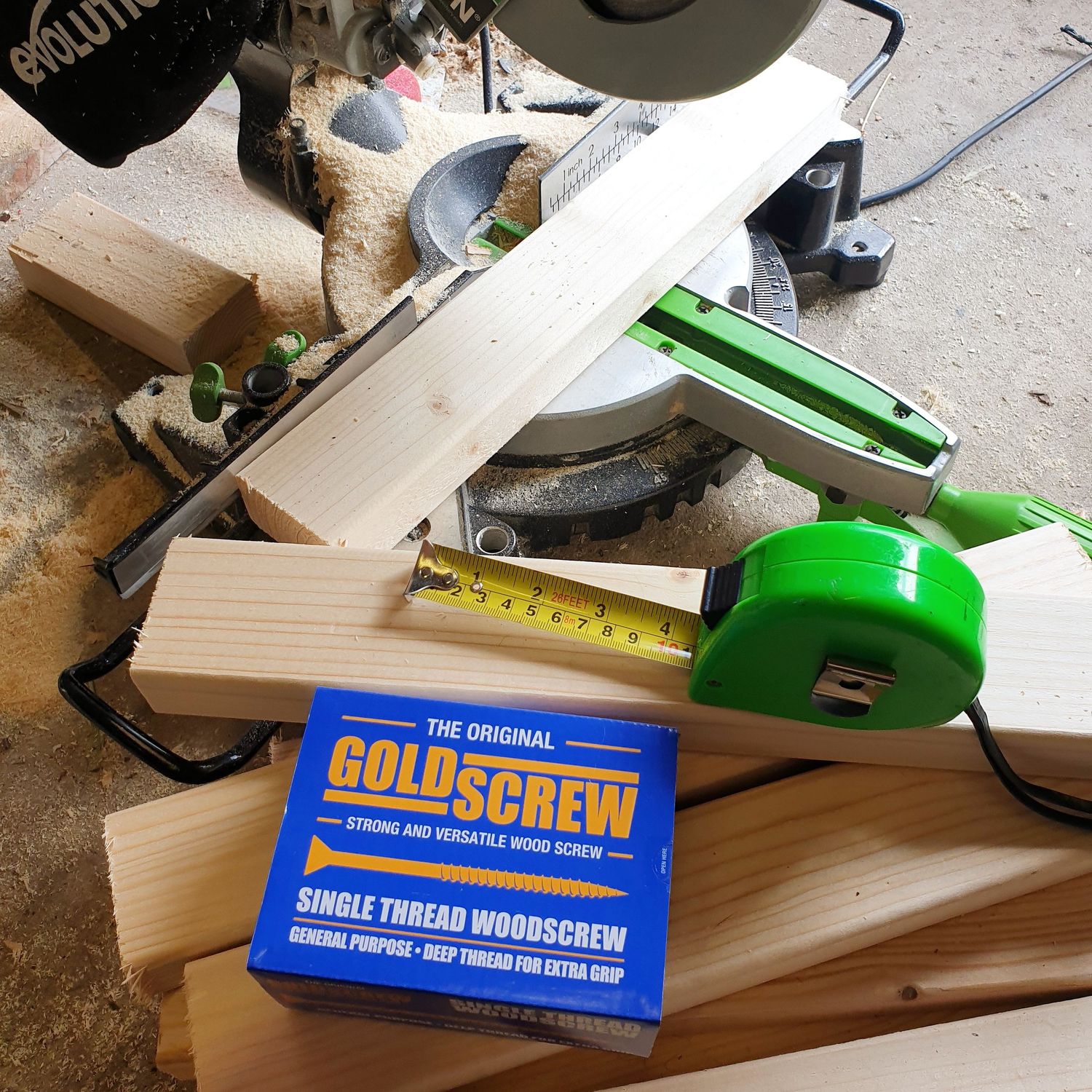 Carpentry tools and materials including measuring tape, wood pieces and Goldscrew box on work surface.