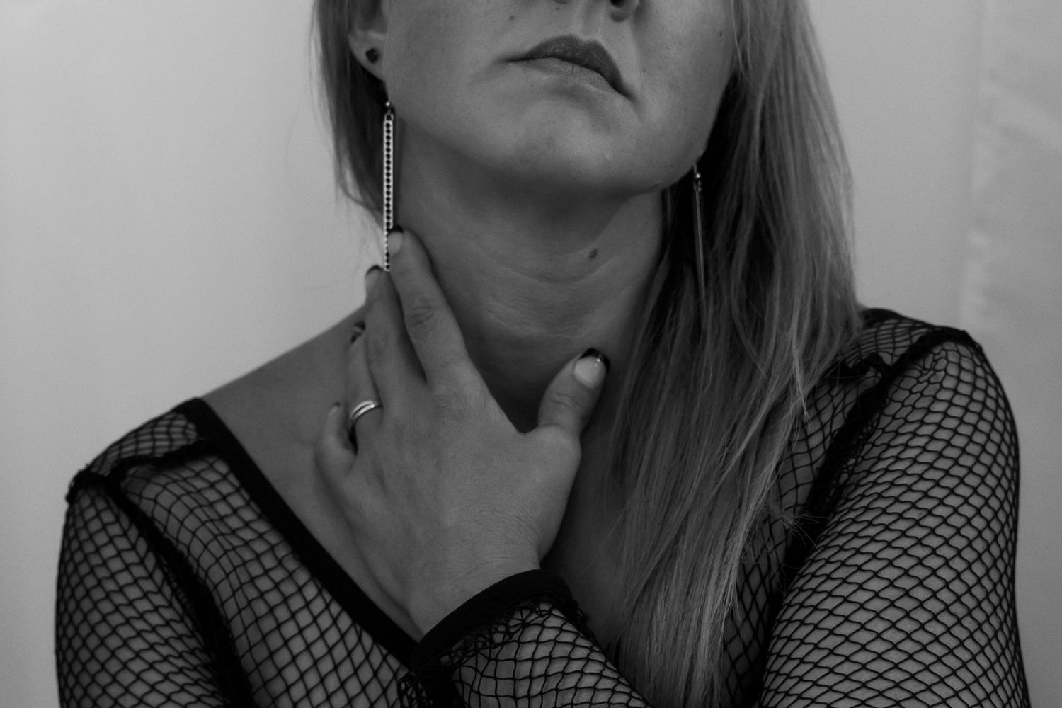 Black and white artistic portrait of a woman in fishnet top with long earrings and ring.