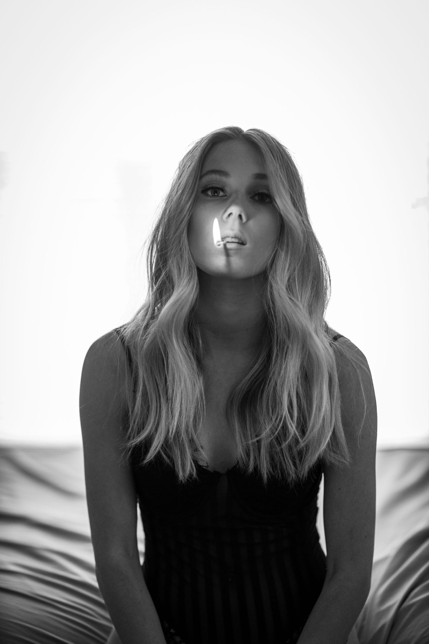 Black and white portrait of blonde woman exhaling smoke while seated indoors.