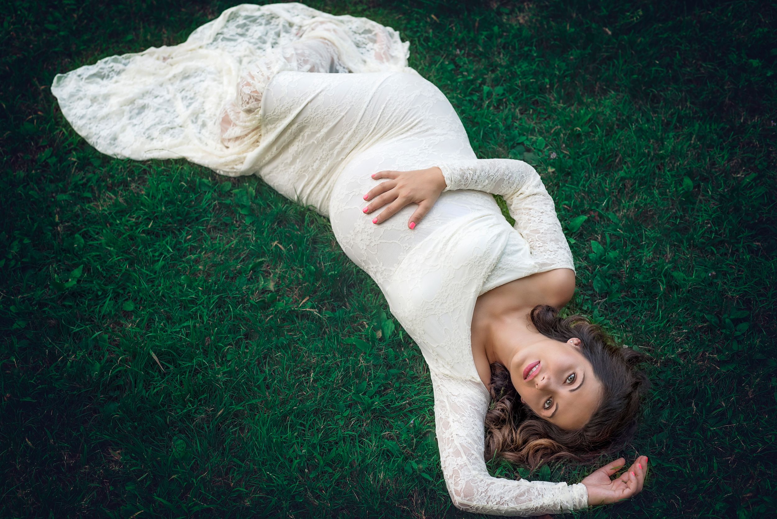 Person in white lace dress lying on green grass with flowing fabric.