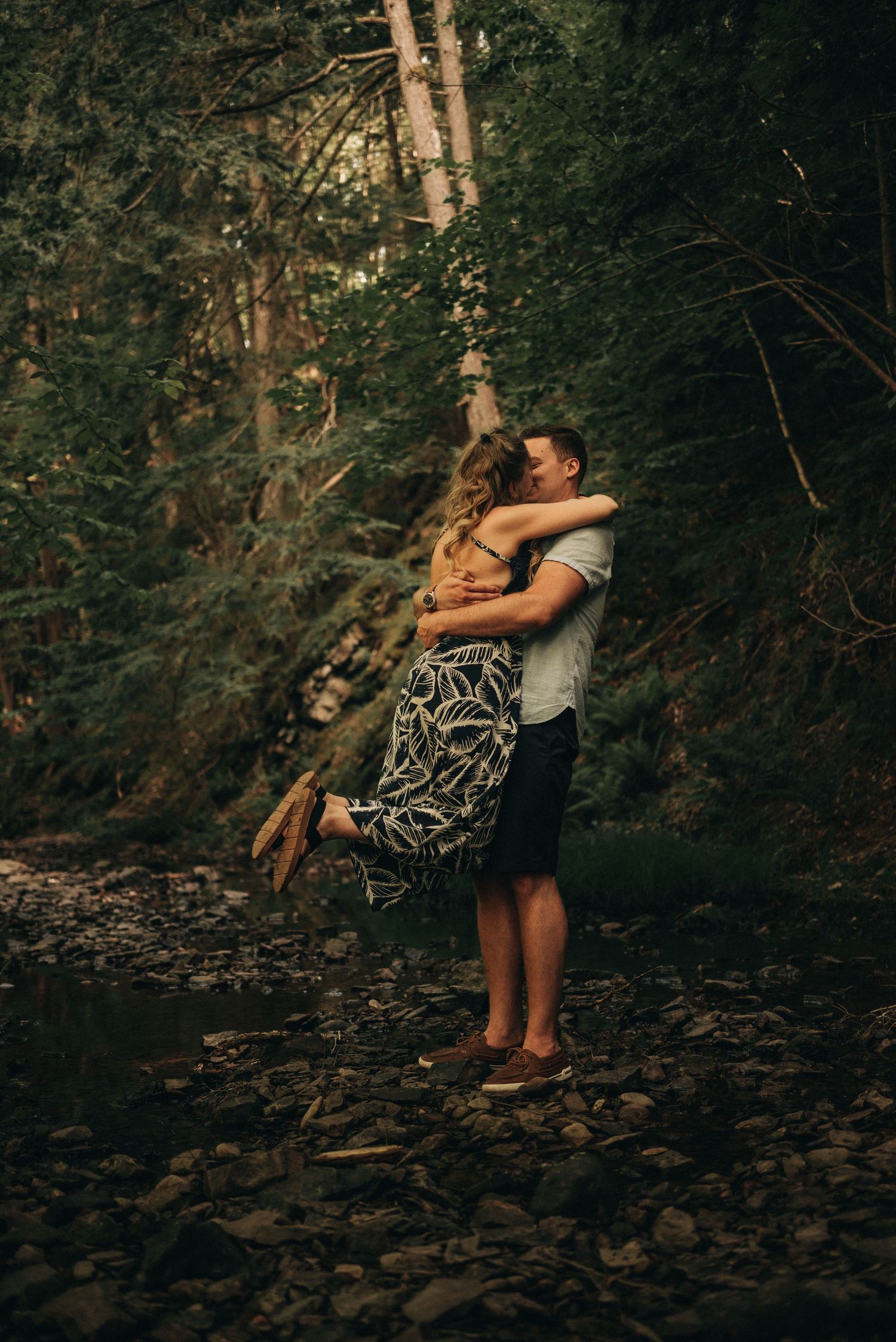 A joyful embrace on a rocky riverbed surrounded by dense forest.