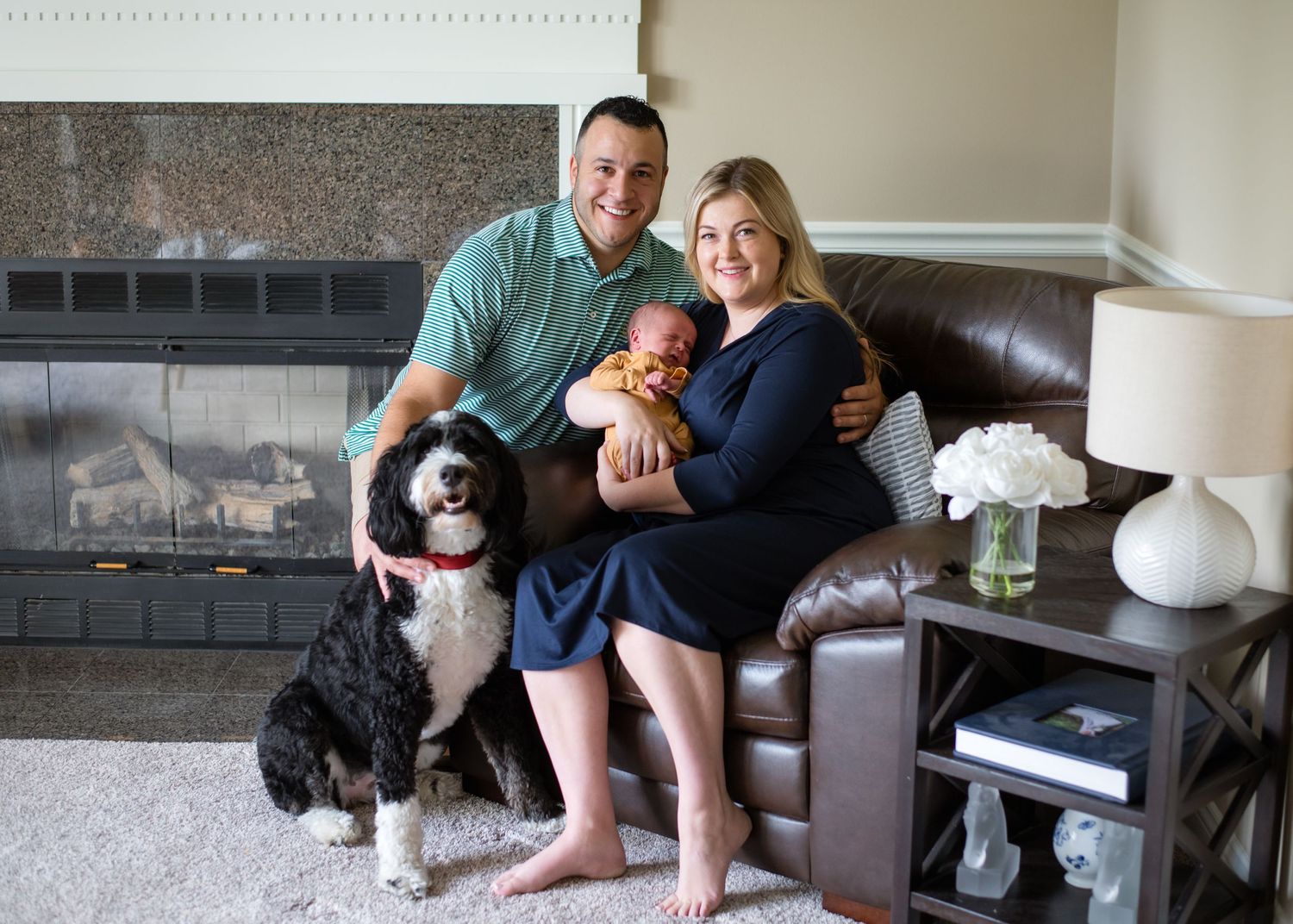 Family sitting on couch near fireplace with black and white dog.