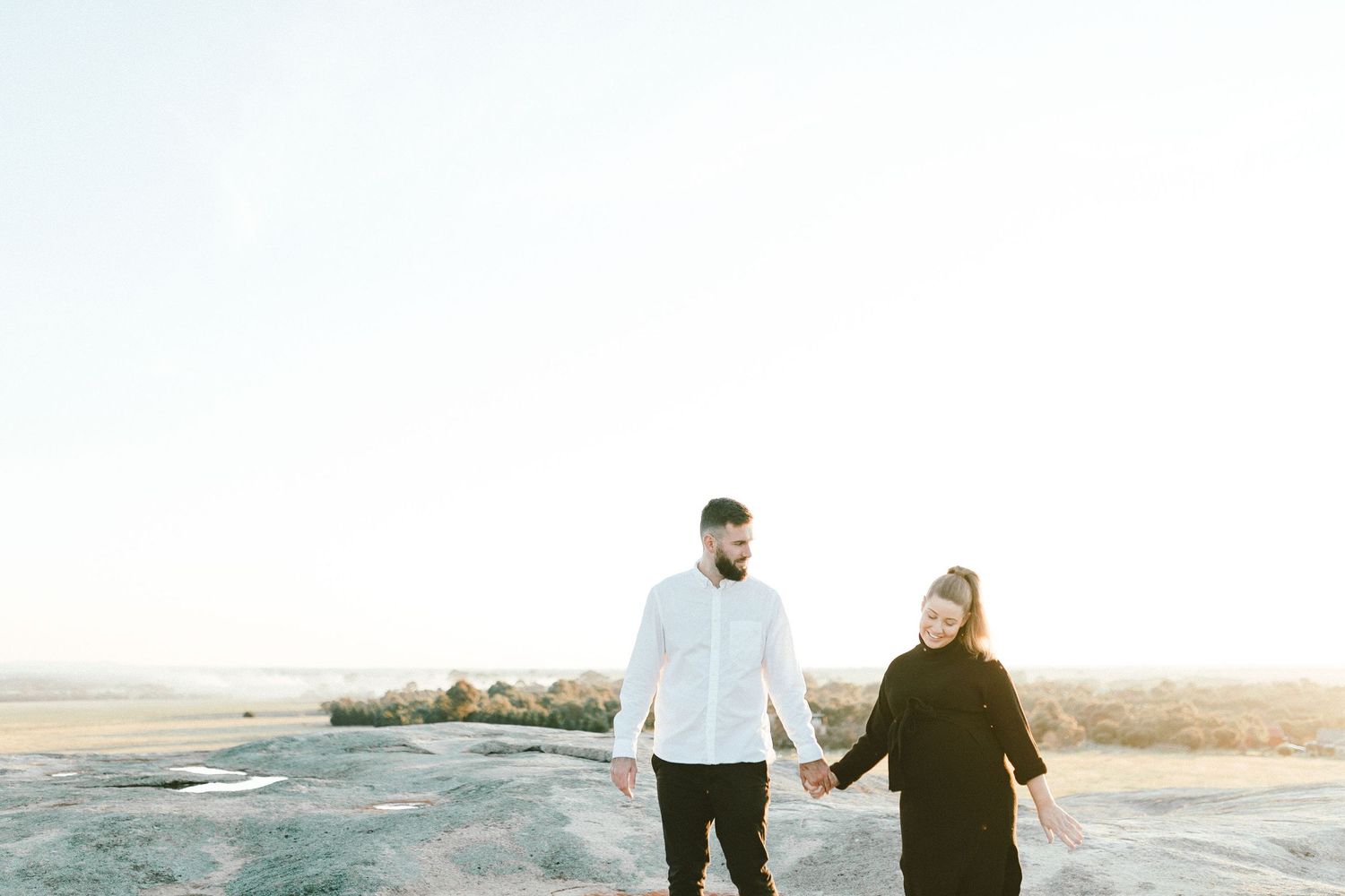 Couple holding hands while walking on rocky terrain during sunset photo session.