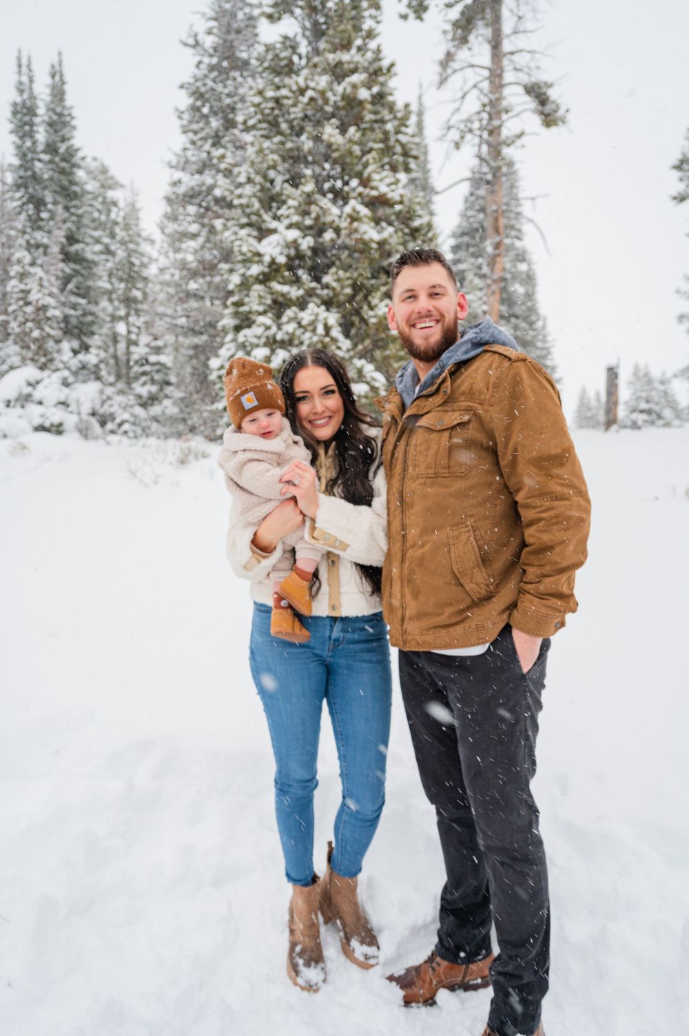 Family portrait in a snowy mountain setting with snow-covered evergreens.