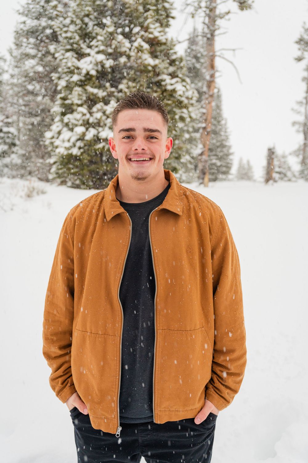Portrait of someone in a brown jacket standing in a snowy winter forest setting.