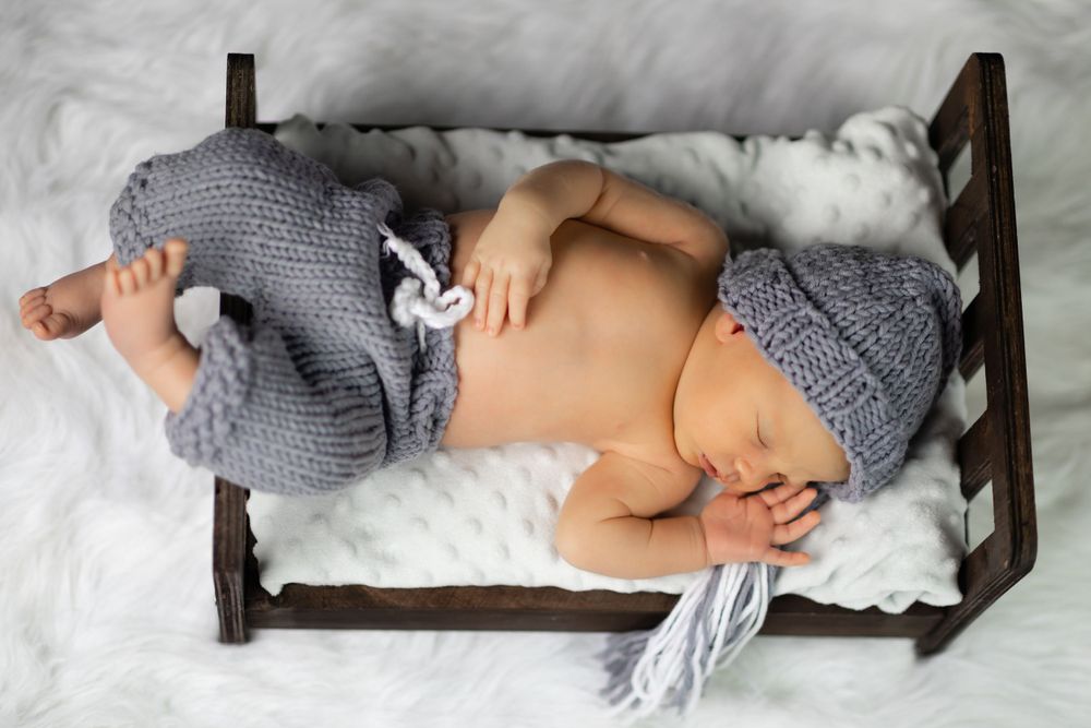 newborn portrait on a a tiny infant bed wearing knitted pajamas and hat