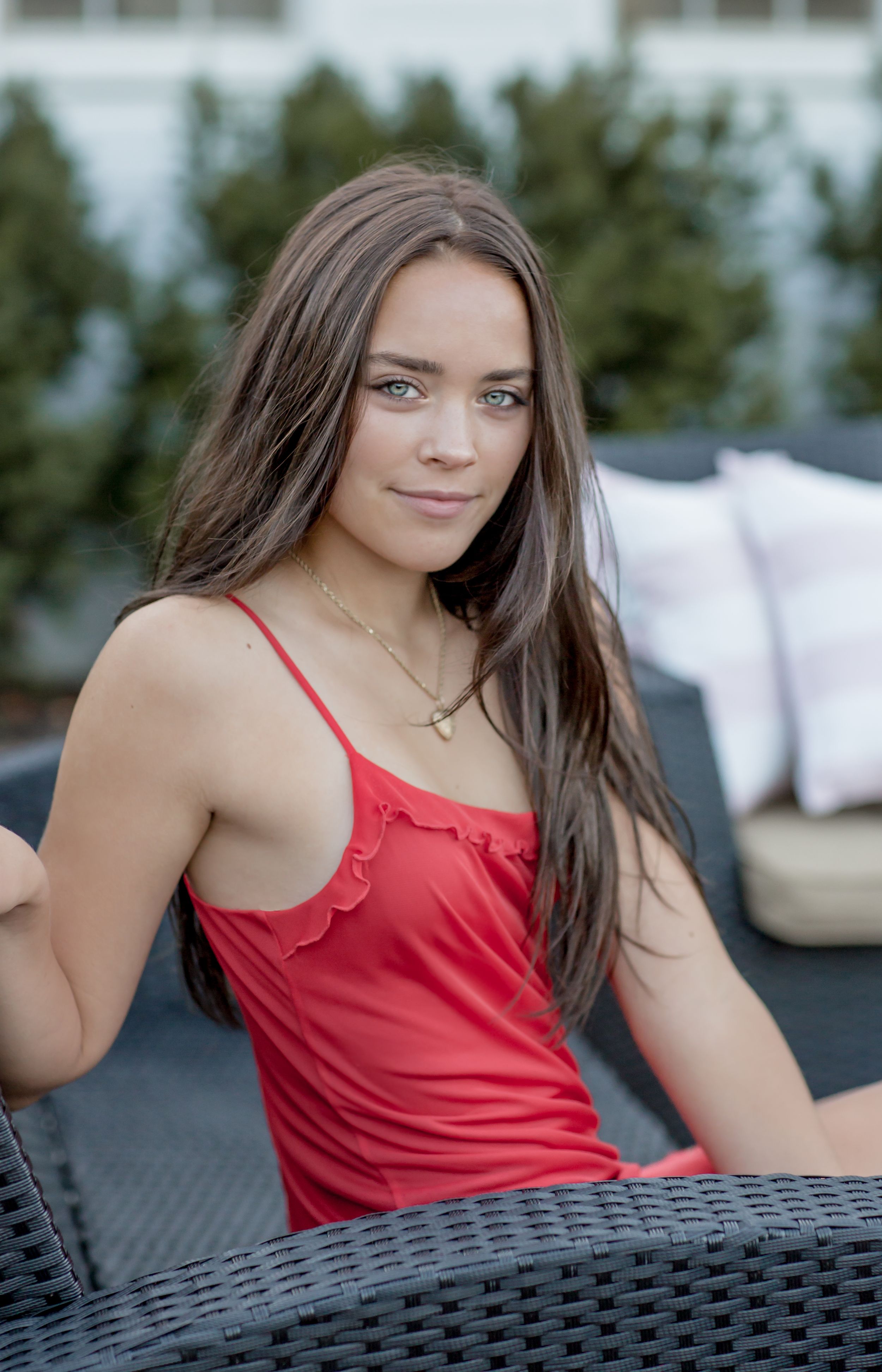 Young woman with long brown hair wearing a red camisole top seated outdoors.