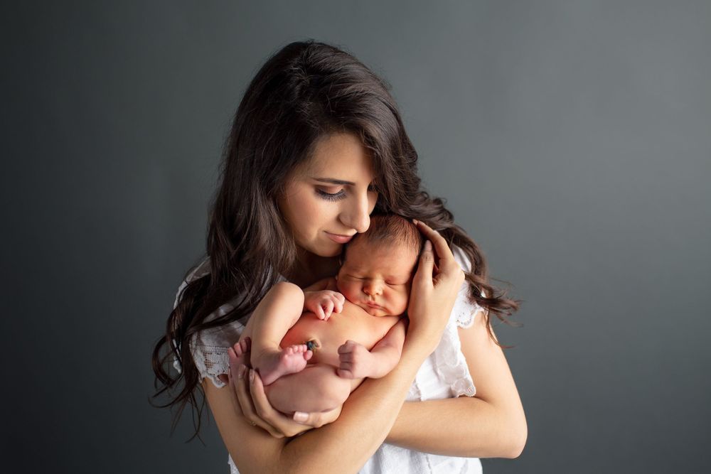 Intimate portrait of parent cradling sleeping newborn baby against dark background.